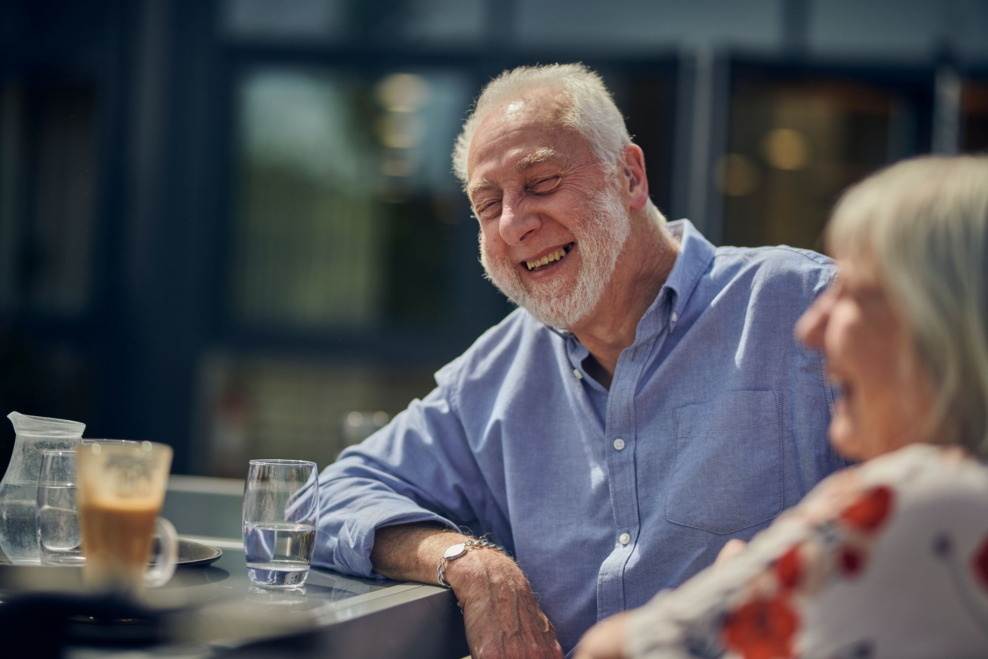Smiling Older Man And Woman Sitting Together Outdoors At Table In The Sunshine