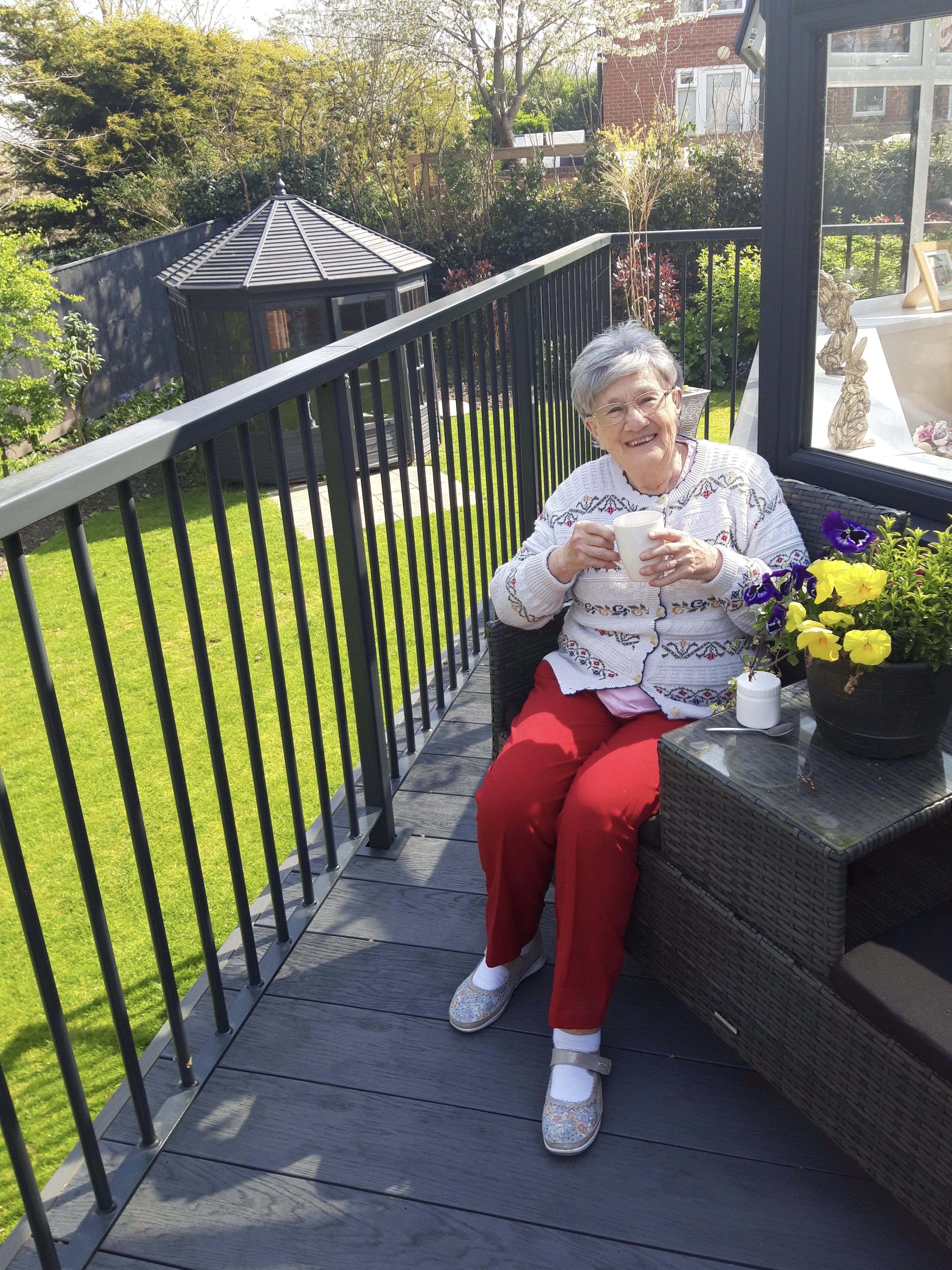 Resident sits smiling with a cup of tea on a balcony at Westbourne House