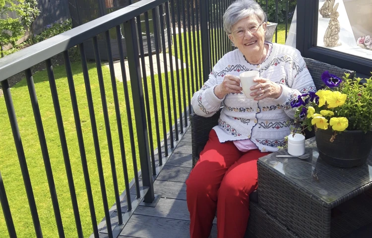 Resident sits smiling with a cup of tea on a balcony at Westbourne House