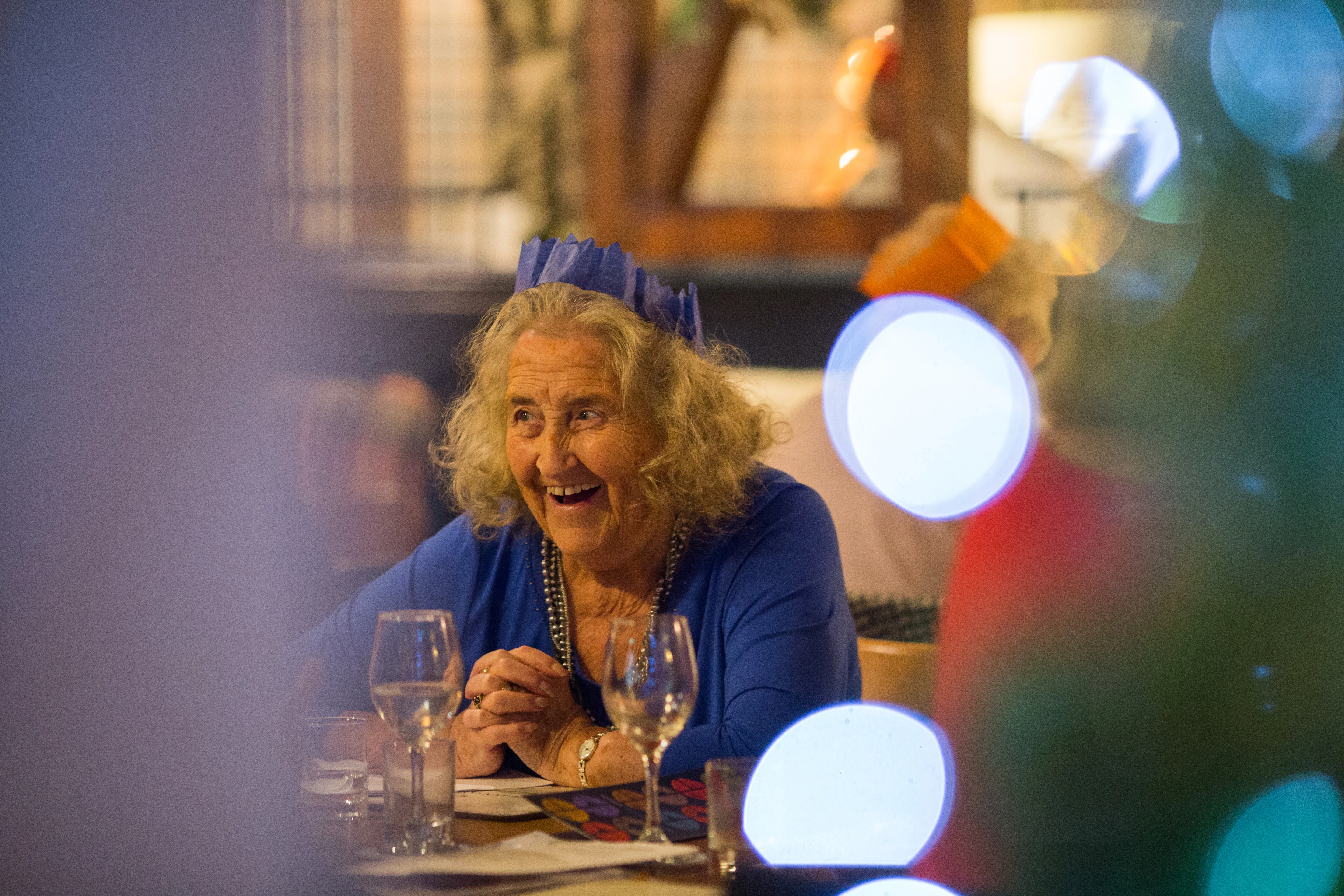 Smiling Older Lady Sitting At Table With Christmas Hat