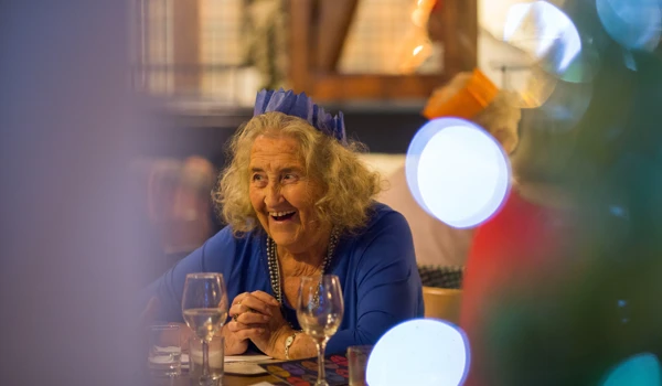 Smiling Older Lady Sitting At Table With Christmas Hat