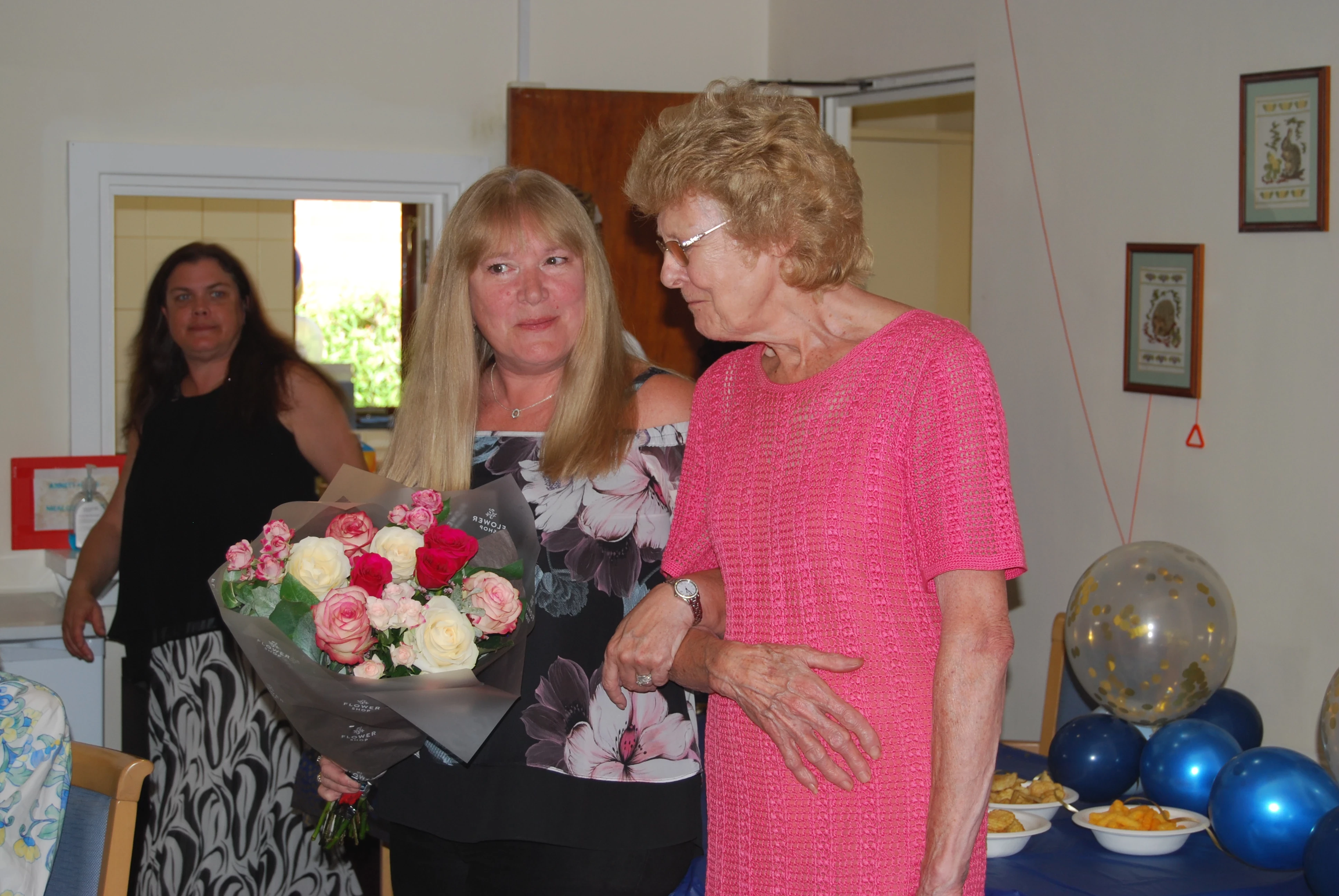 2 women arm in arm one with a bunch of flowers