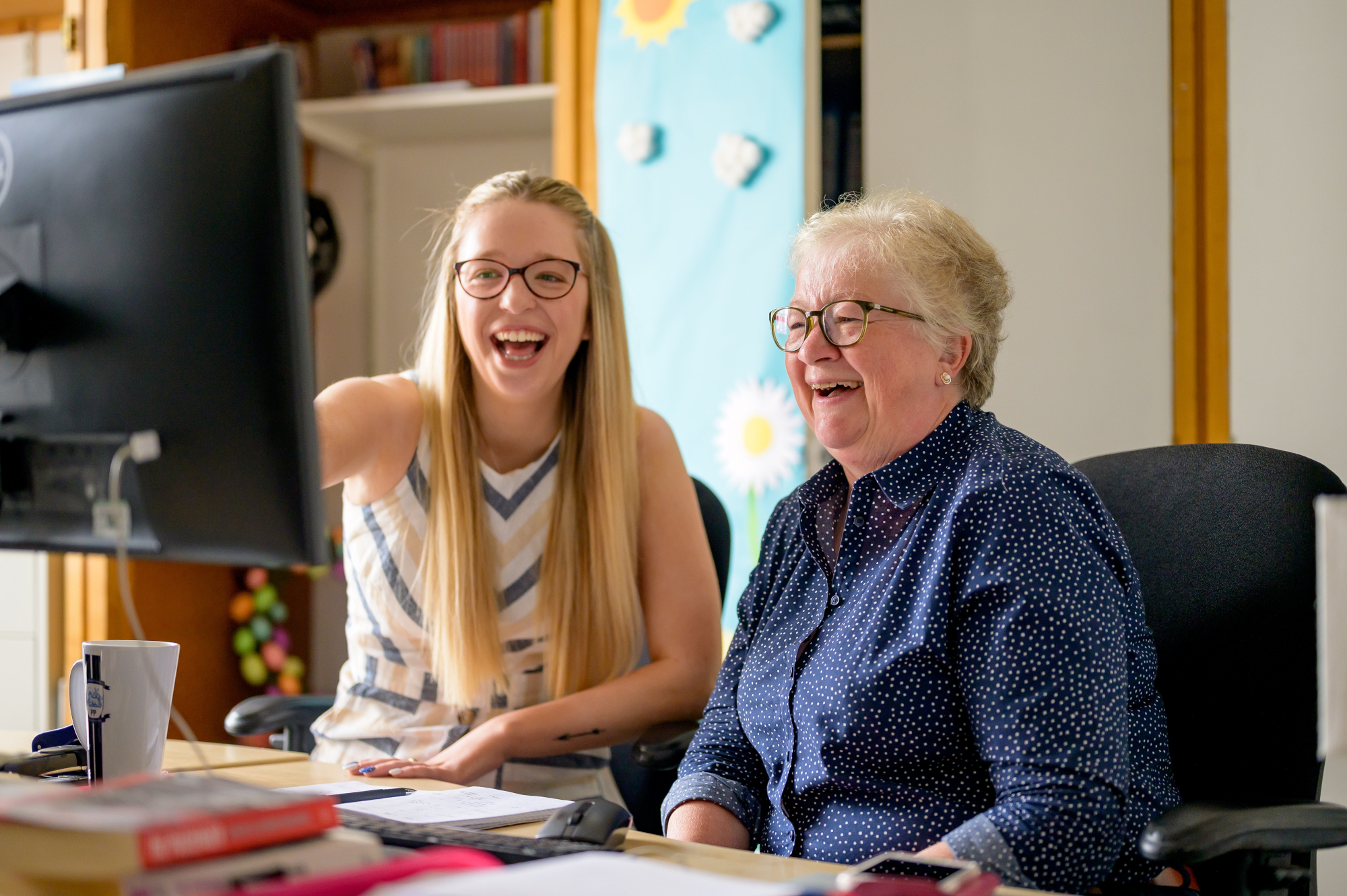 Smiling Woman Sitting With Older Woman Looking At A Computer Screen