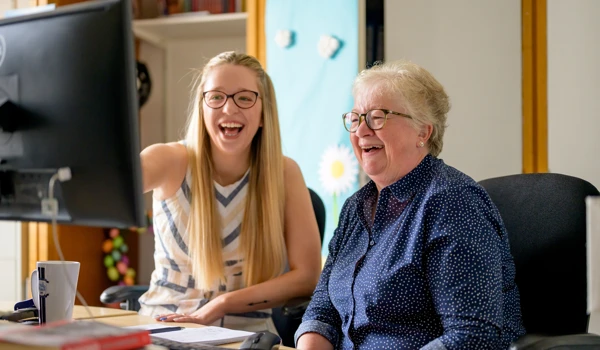 Smiling Woman Sitting With Older Woman Looking At A Computer Screen