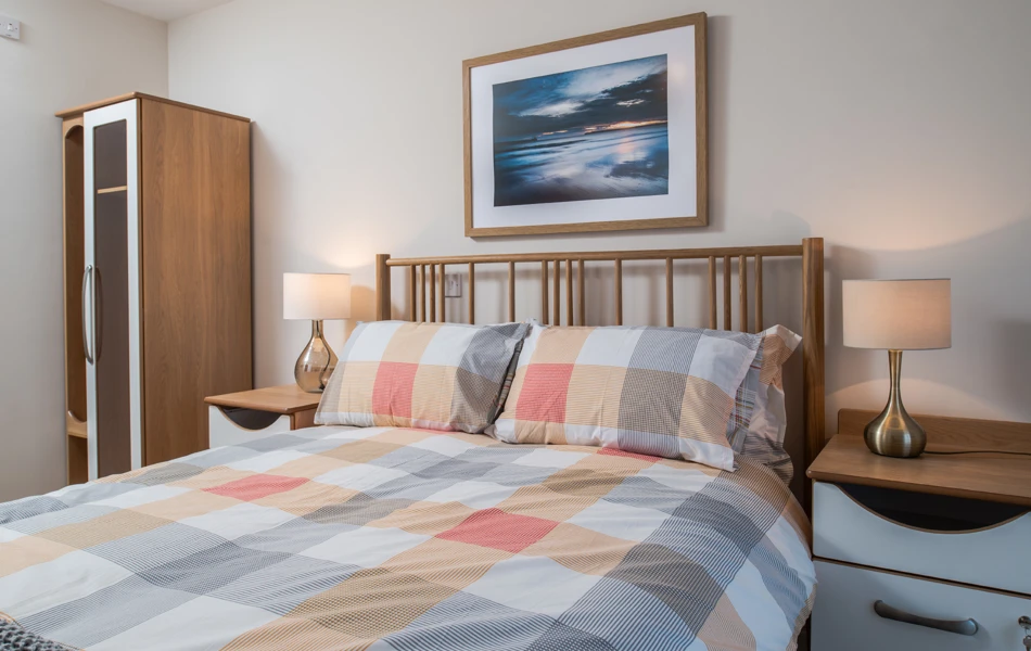 Double bed with a checkered bedspread and bedside cabinets at Hope Bank View