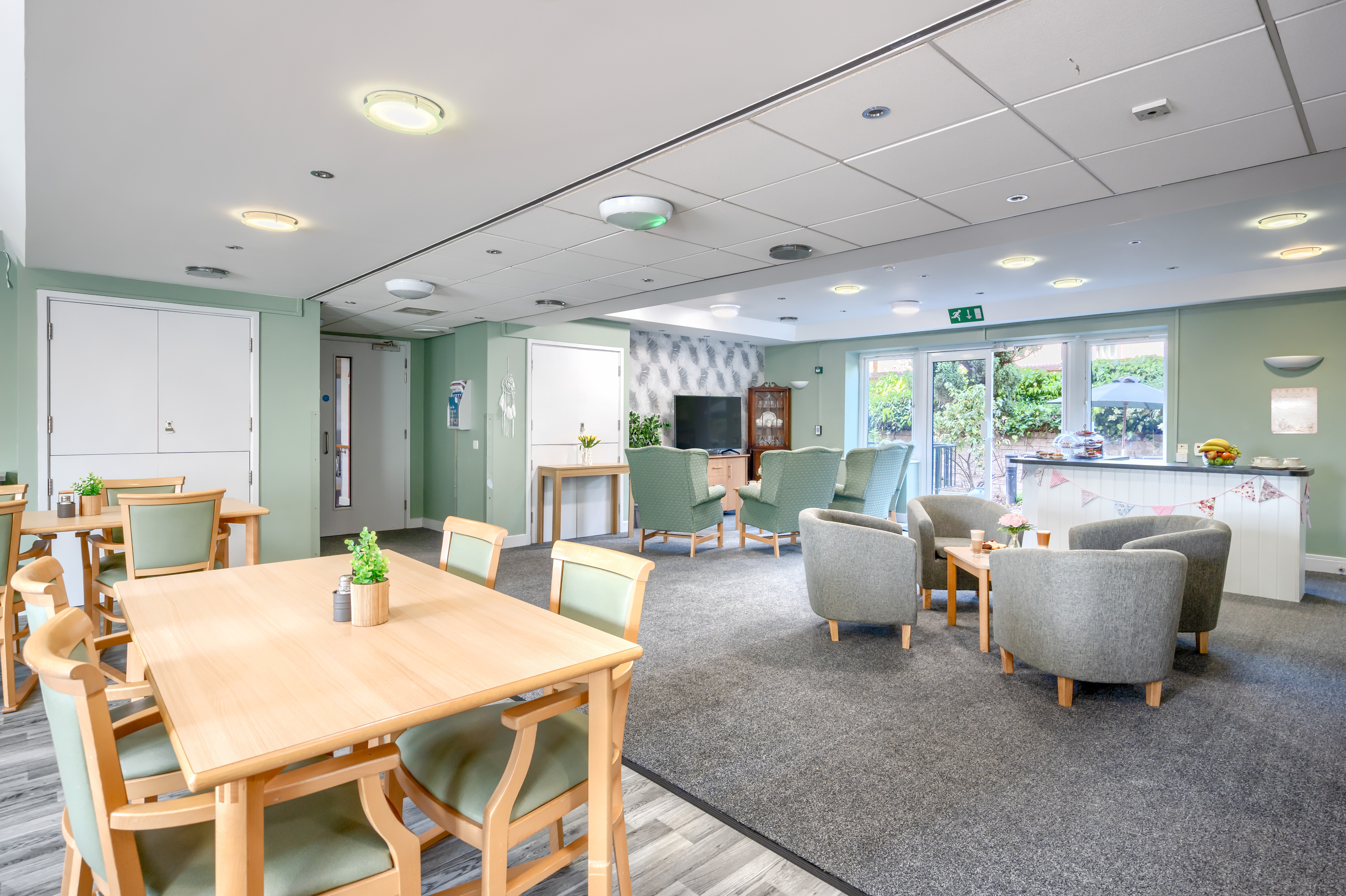 Sandwood Care Home in Nottingham offers a welcoming and stimulating community centre for residents featuring comfortable chairs, tables and a central television, perfect for socialising and activities.jpg