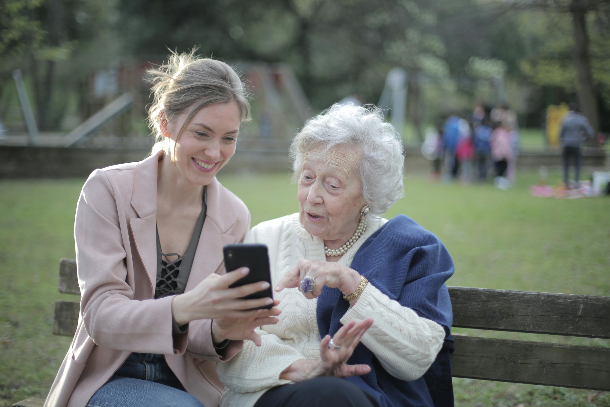 Older Woman And Younger Woman Looking At Phone Together On Park Bench