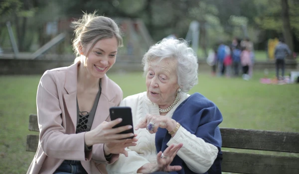 Older Woman And Younger Woman Looking At Phone Together On Park Bench