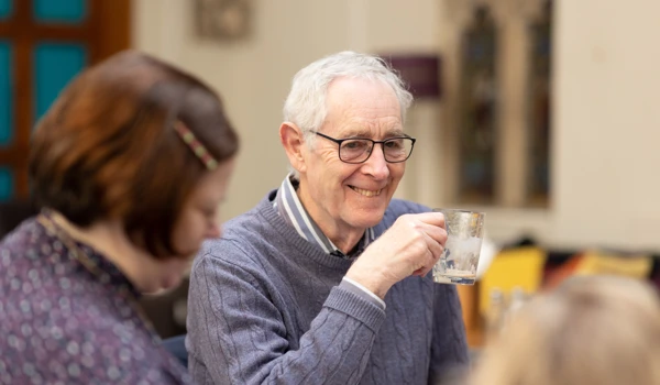 Older Man Smiling With Coffee At Table With Others