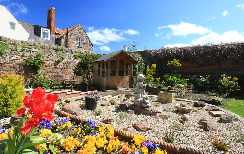 A stunning rockery in the garden with a summer house and bright flowers