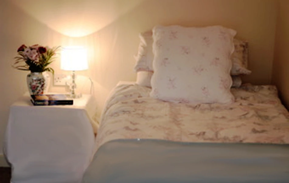 A bedroom with a lamp and flowers on the bedside table