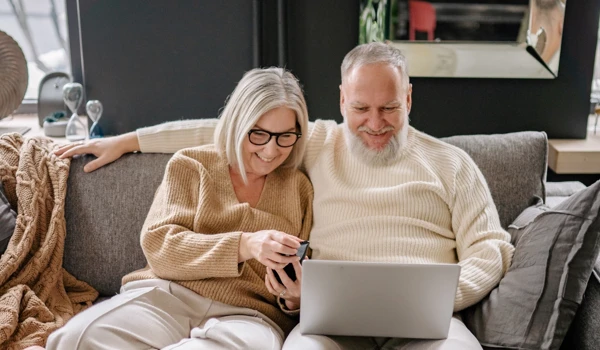 Smiling Older Couple Sitting On Sofa Looking On Laptop