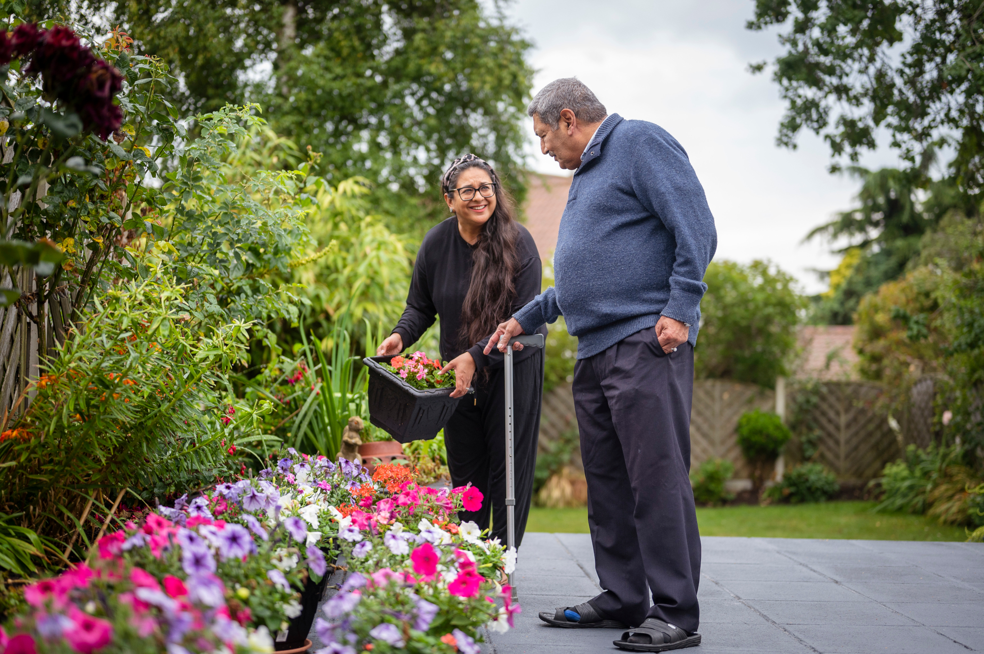 Woman Holding A Plant Pot In The Garden With Older Man