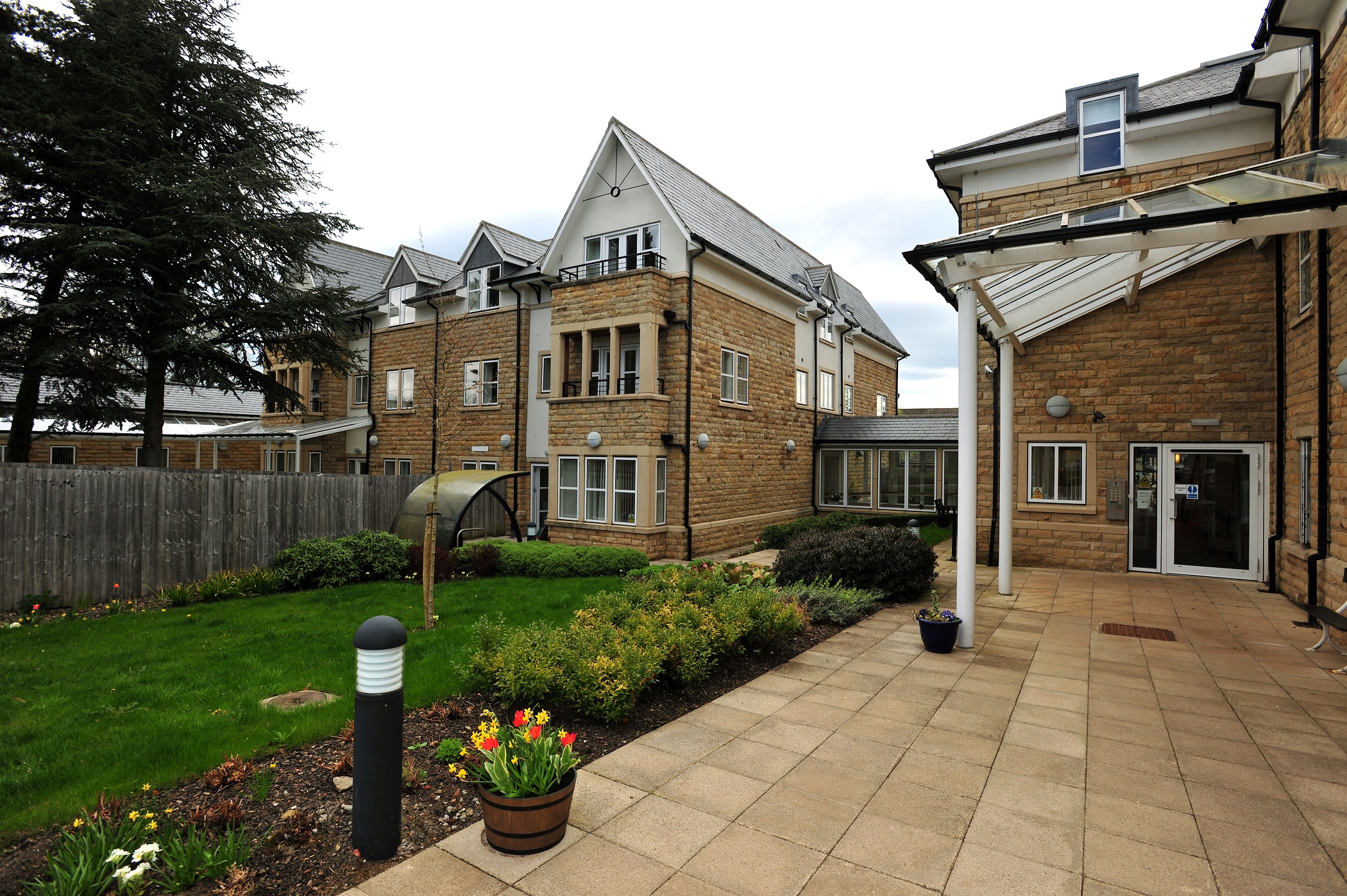 The garden and patio area with a pot of flowers in the foreground of Abbeyfield The Beeches