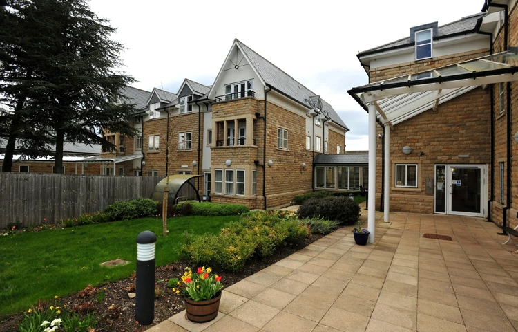 The garden and patio area with a pot of flowers in the foreground of Abbeyfield The Beeches