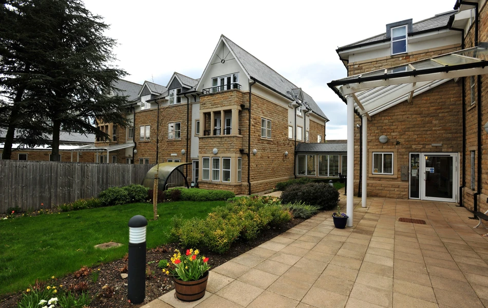 The garden and patio area with a pot of flowers in the foreground of Abbeyfield The Beeches
