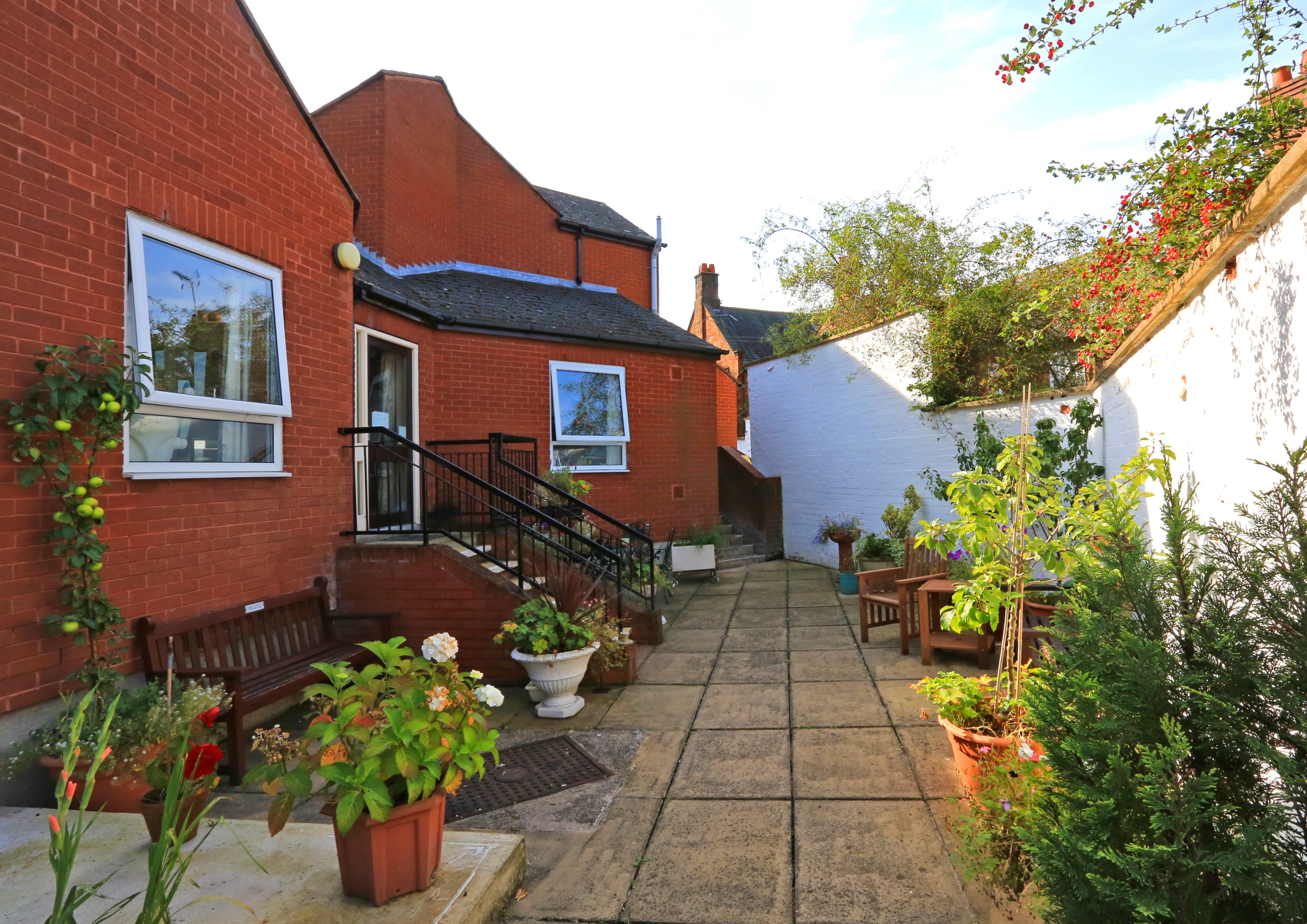 A paved rear garden with pots of plants and seating areas