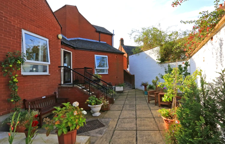 A paved rear garden with pots of plants and seating areas