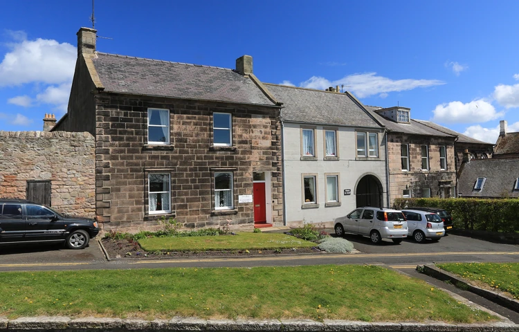The front of a small stone house with grassed areas outside