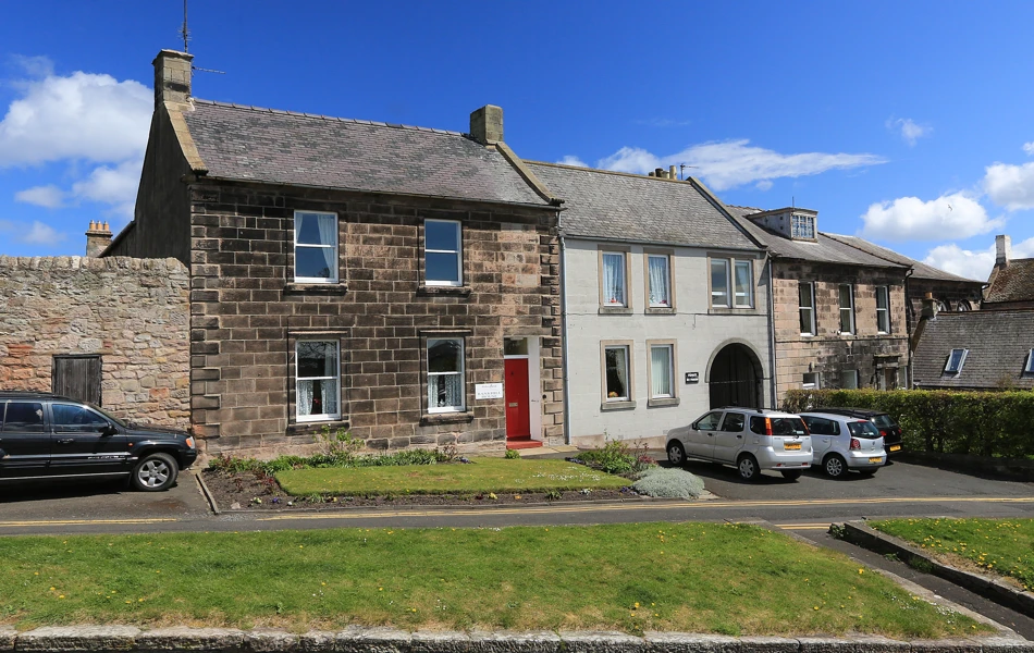The front of a small stone house with grassed areas outside
