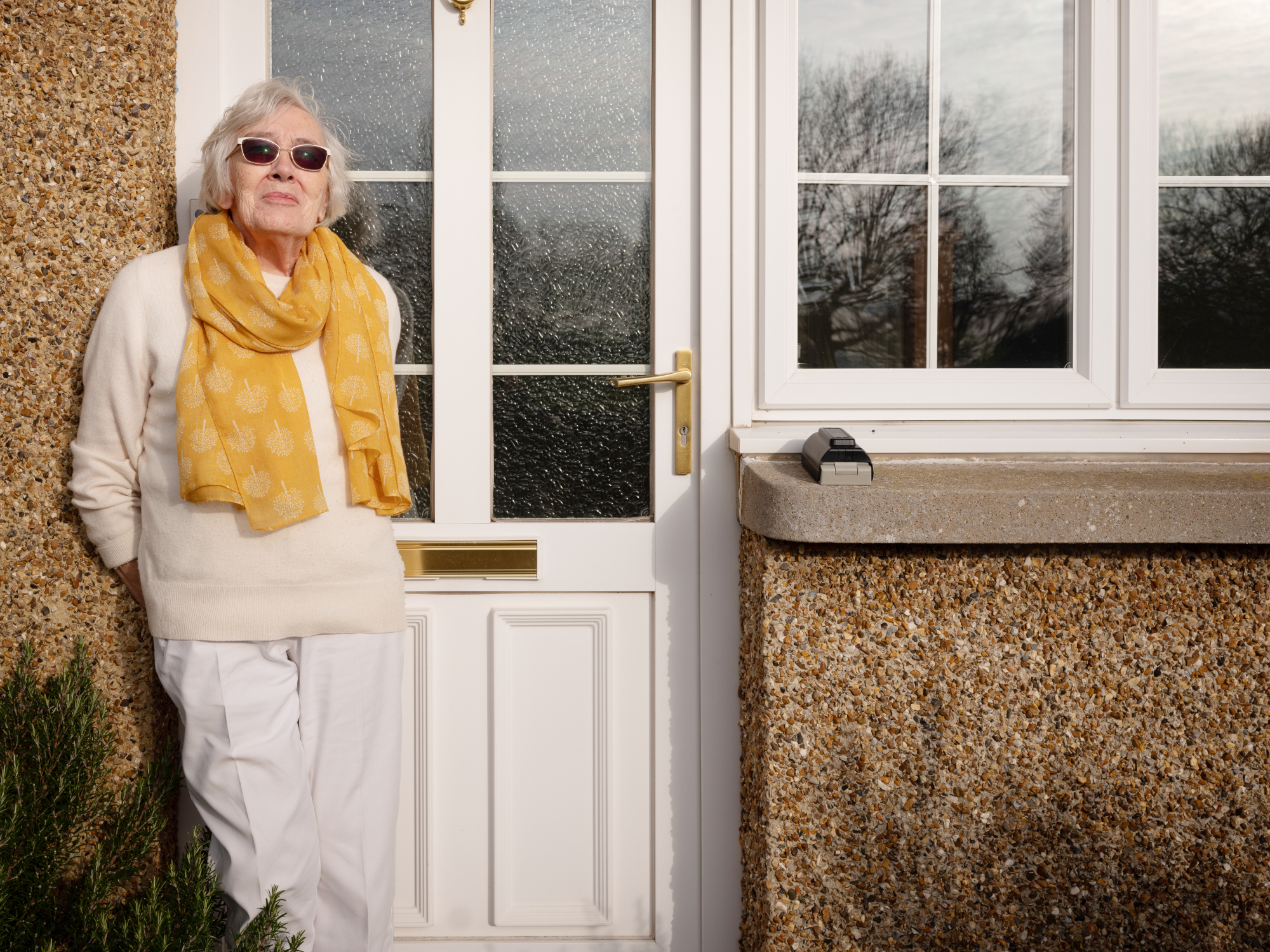 Smiling Older Woman Leaning On Front Door Enjoying The Sunshine