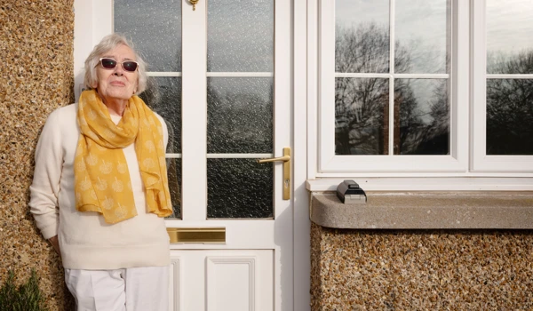 Smiling Older Woman Leaning On Front Door Enjoying The Sunshine