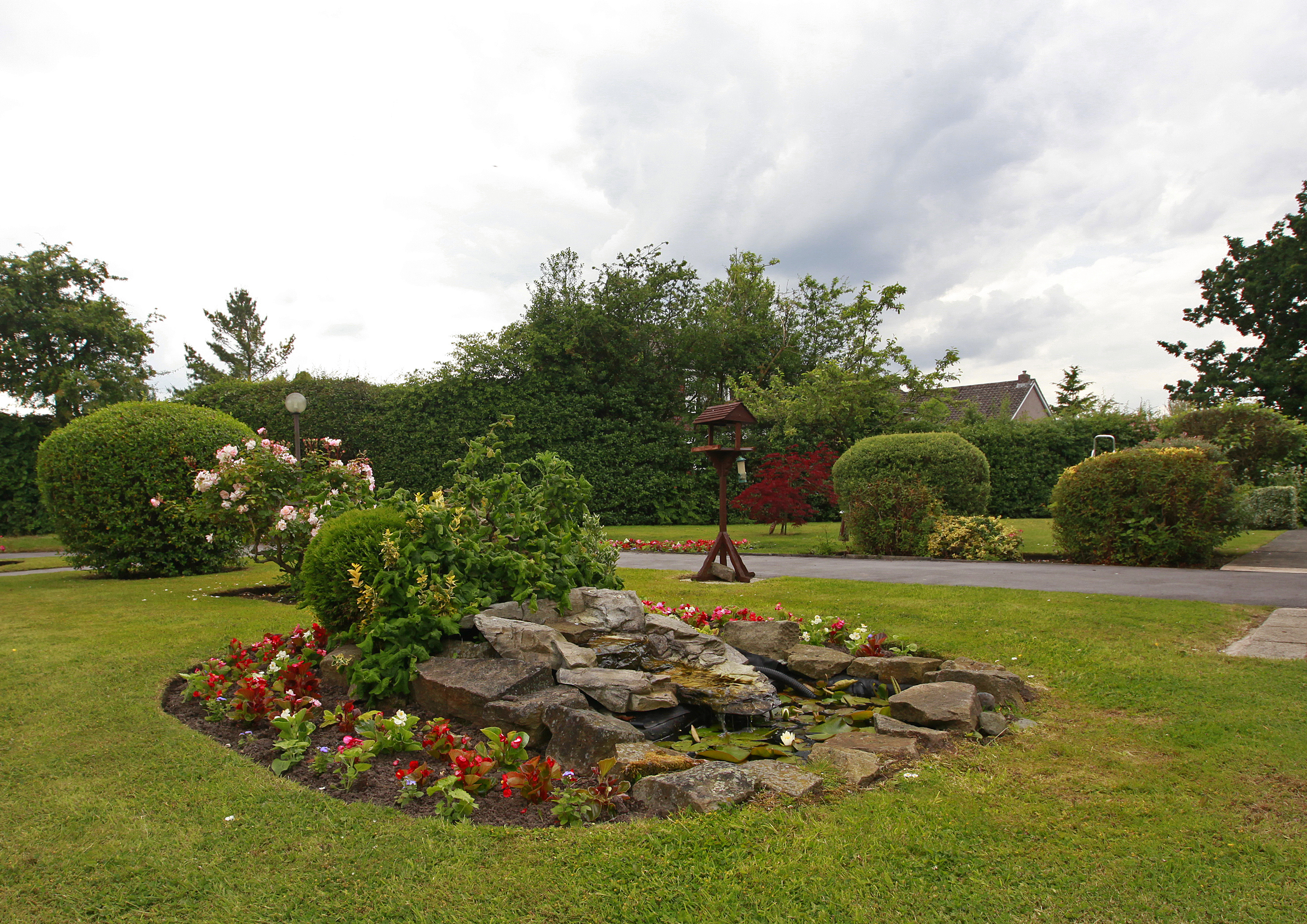 A rockery in the centre of the garden with a bird table on the grass