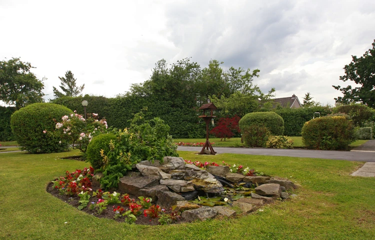 A rockery in the centre of the garden with a bird table on the grass