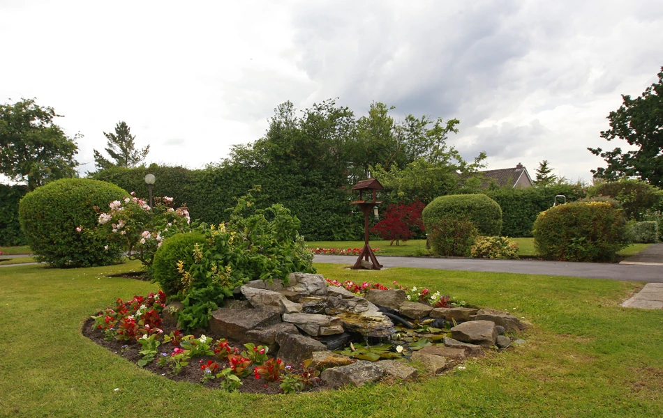 A rockery in the centre of the garden with a bird table on the grass