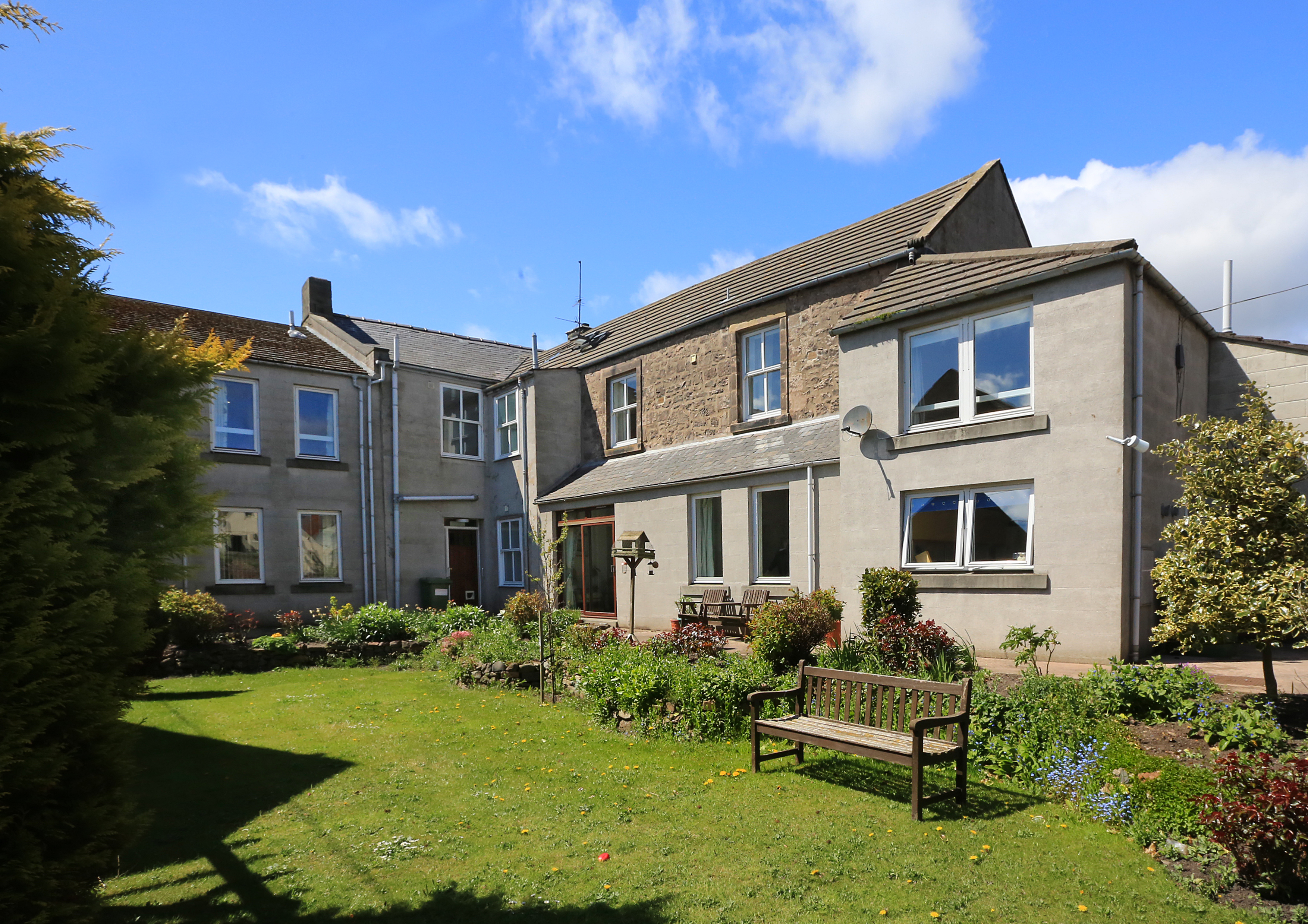 A bright garden to the rear of the house with a park bench