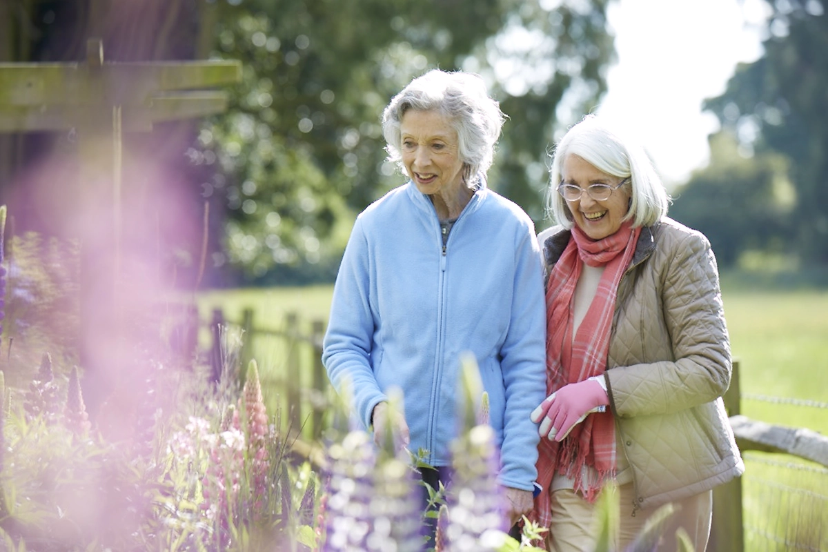 Two Older Women Admiring The Plants In The Garden