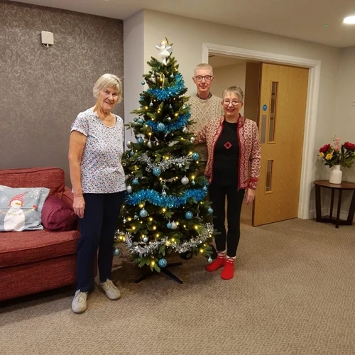 3 people standing next to a Christmas tree