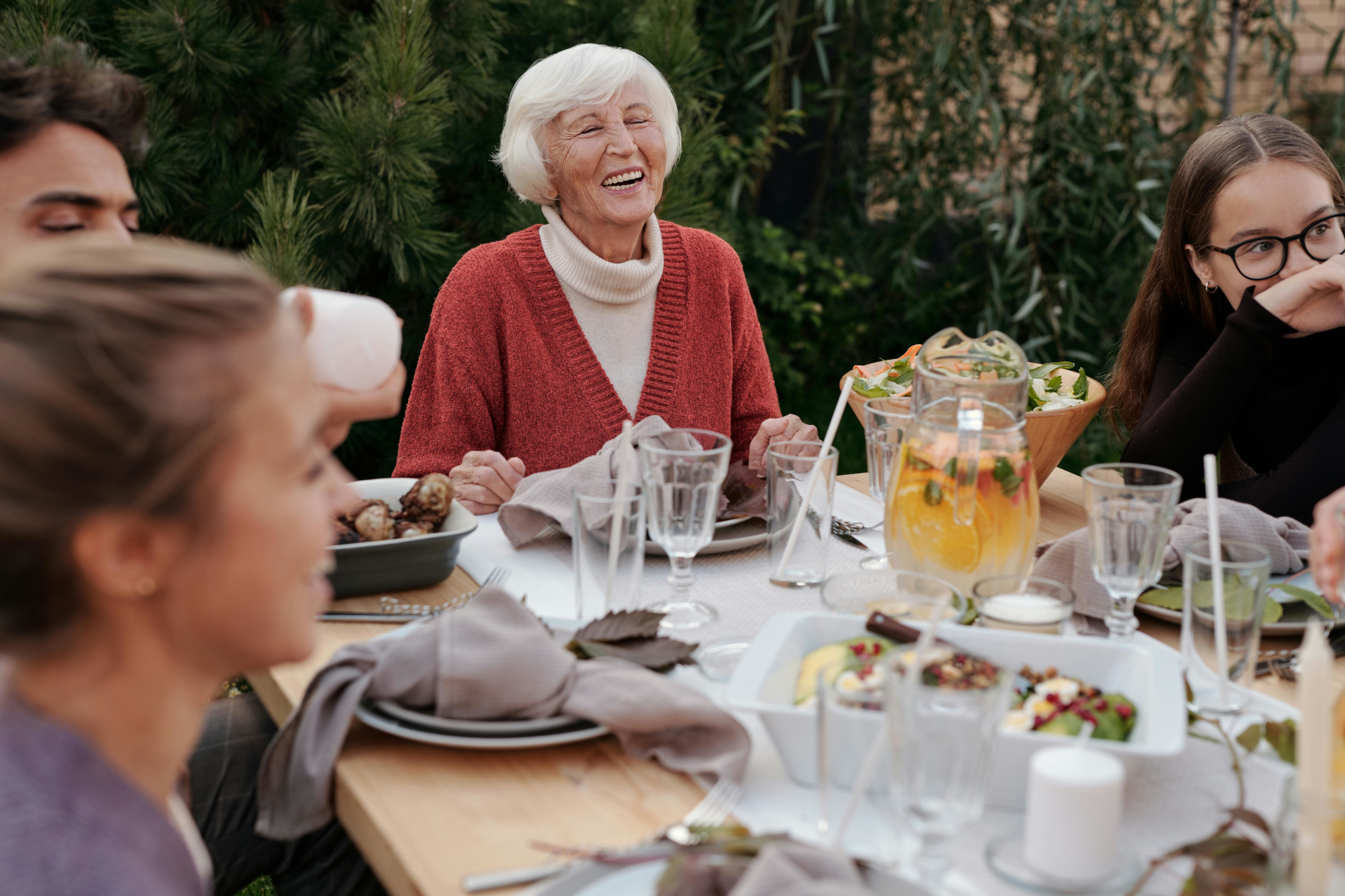 Older Woman With Family And Friends Eating Round The Table Together