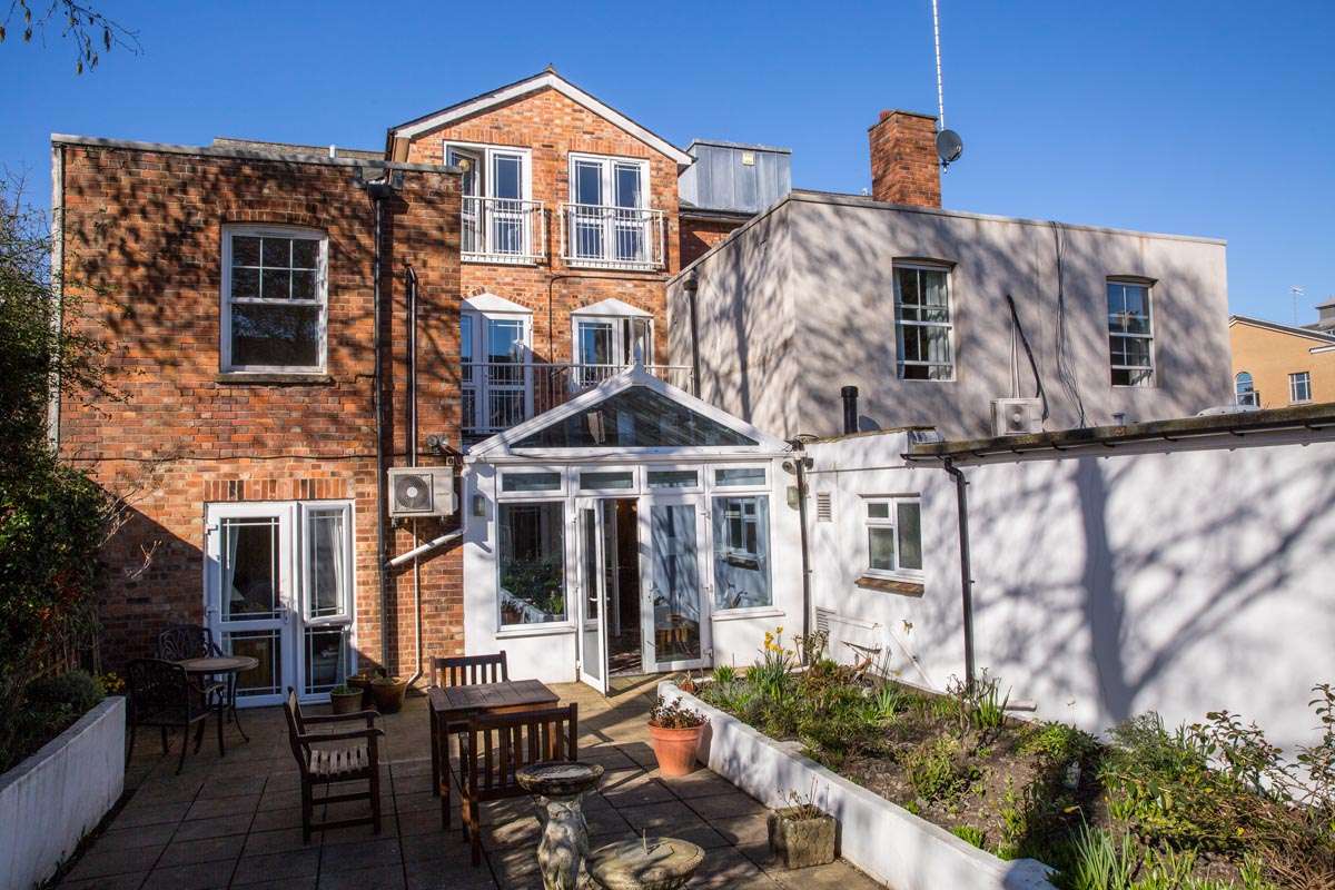 Back exterior of Abbeyfield House, with patio area with tables and chairs and a raised flowerbeds