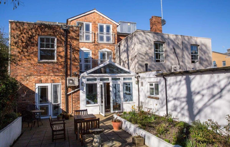 Back exterior of Abbeyfield House, with patio area with tables and chairs and a raised flowerbeds