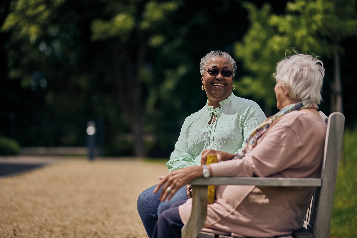 Two Women Sitting Together On Bench Enjoying A Conversation