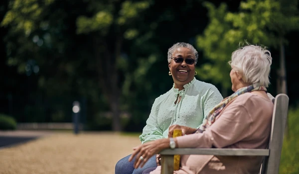 Two Women Sitting Together On Bench Enjoying A Conversation