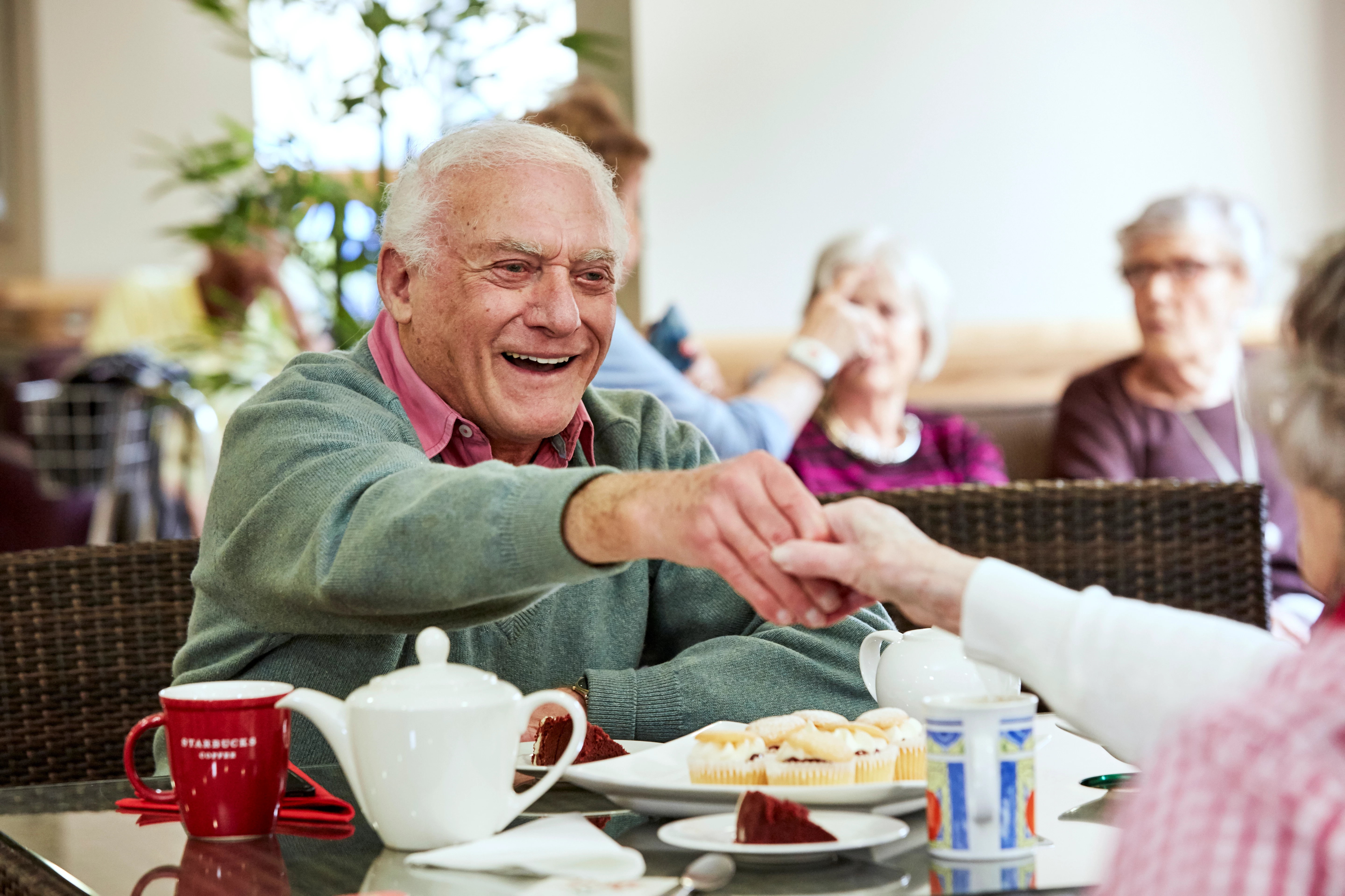 Smiling Older Man Enjoying Tea And Cakes With Others