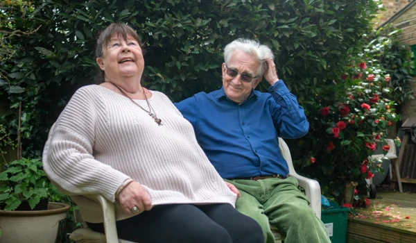 Older Woman And Man Sitting Together On A Bench In The Garden