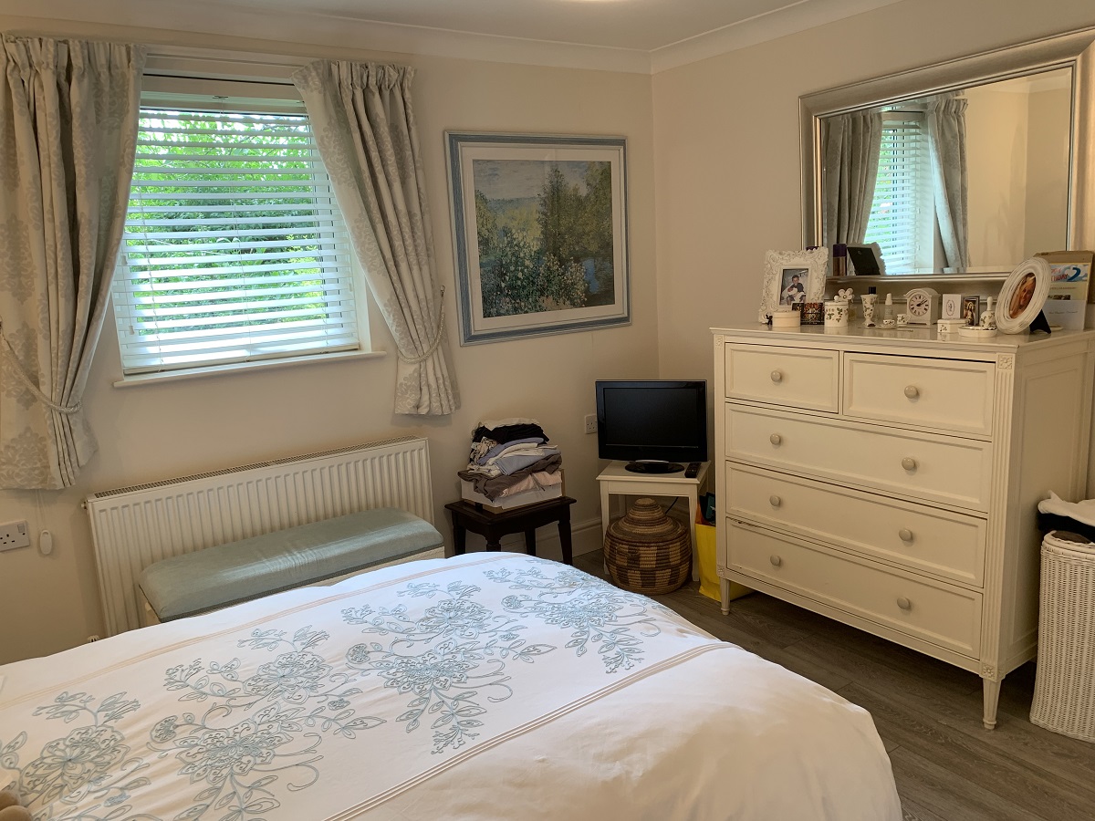 A large resident bedroom at The Firs Complex with a chest of draws, small tv and bed