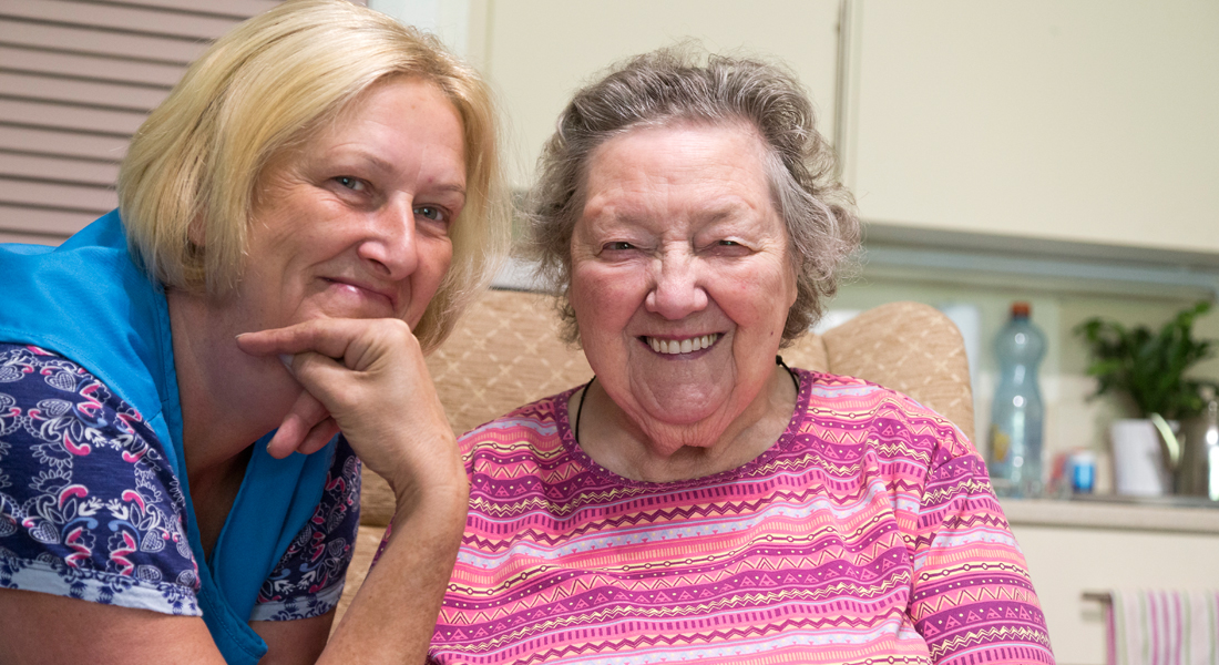 Two women sat smiling for a photo in the kitchen