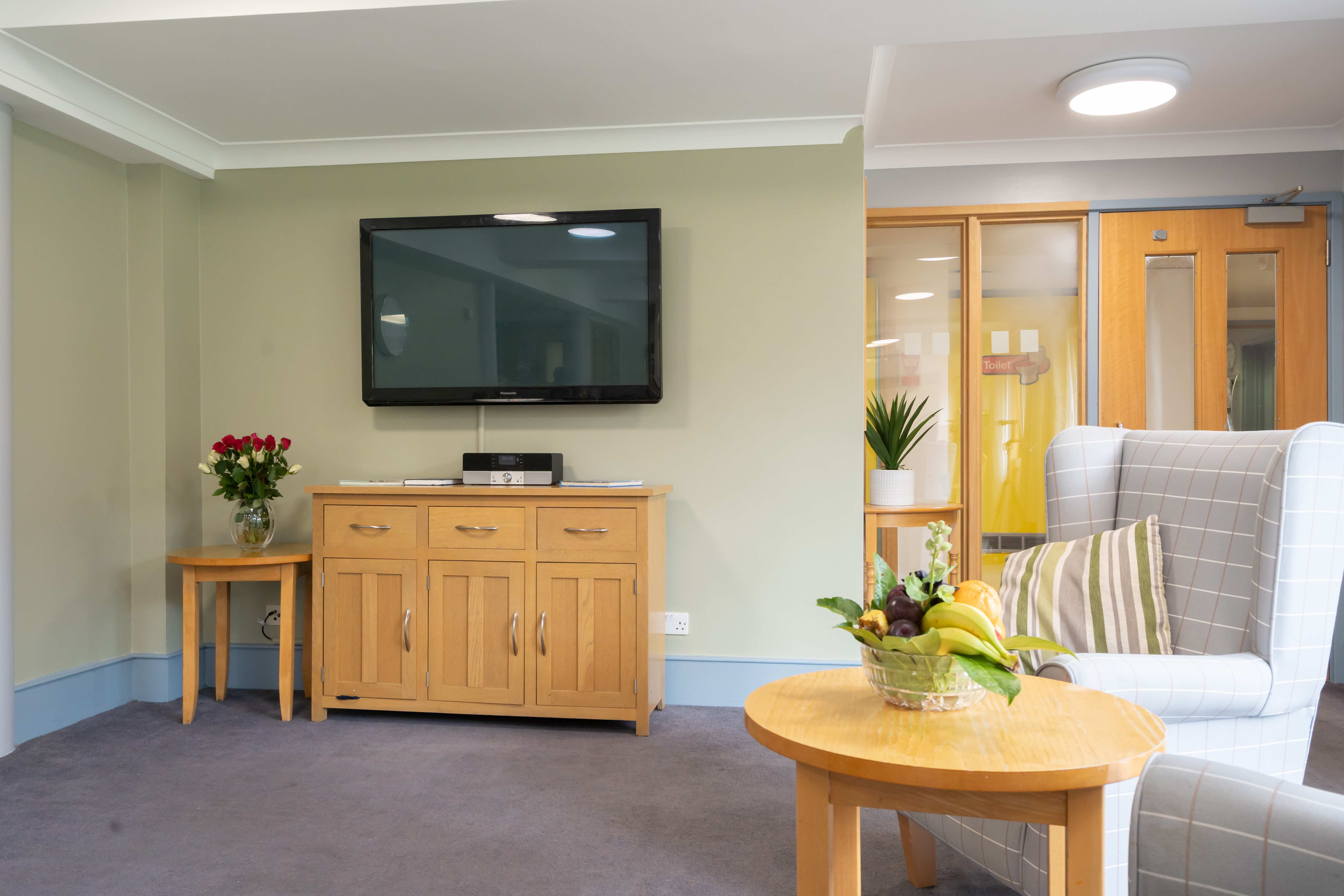 TV and chairs in lounge with fruit bowl at Abbeyfield House, New Malden