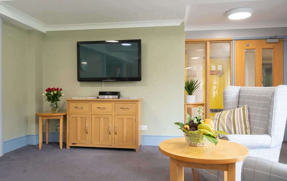 TV and chairs in lounge with fruit bowl at Abbeyfield House, New Malden