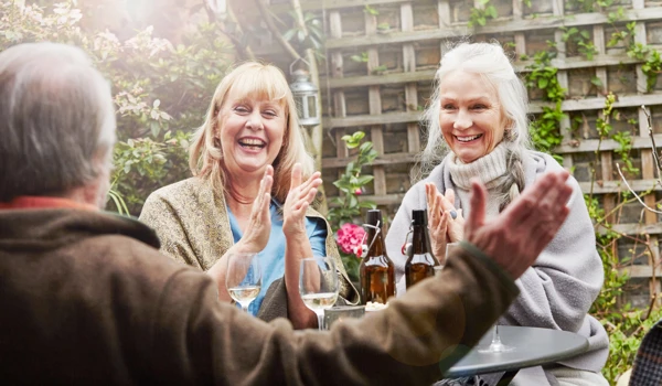 Happy Group Of People Sitting Around Having Drinks In The Garden