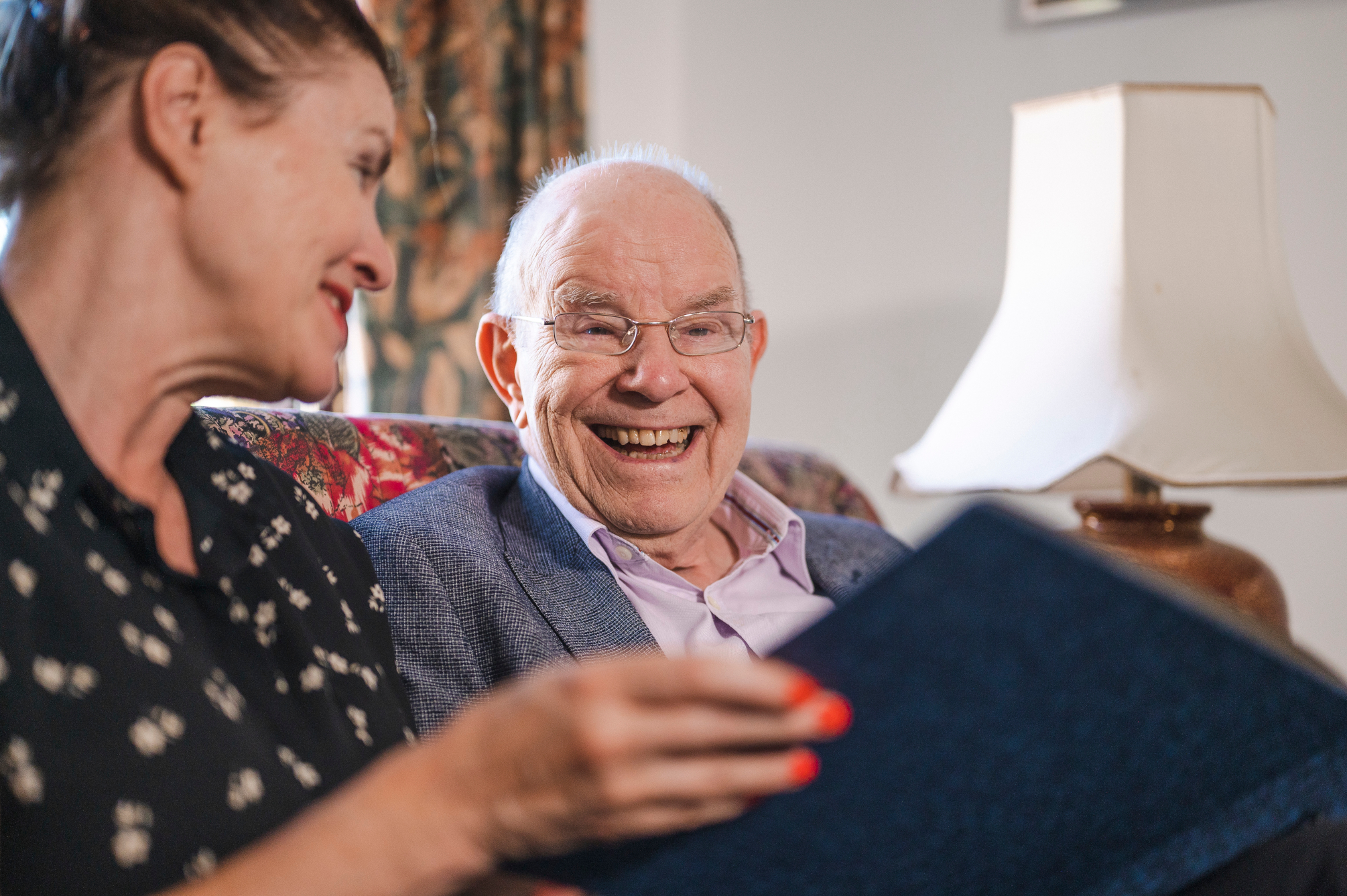 Smiling Older Man And Woman Sitting On Sofa Looking At Photo Album