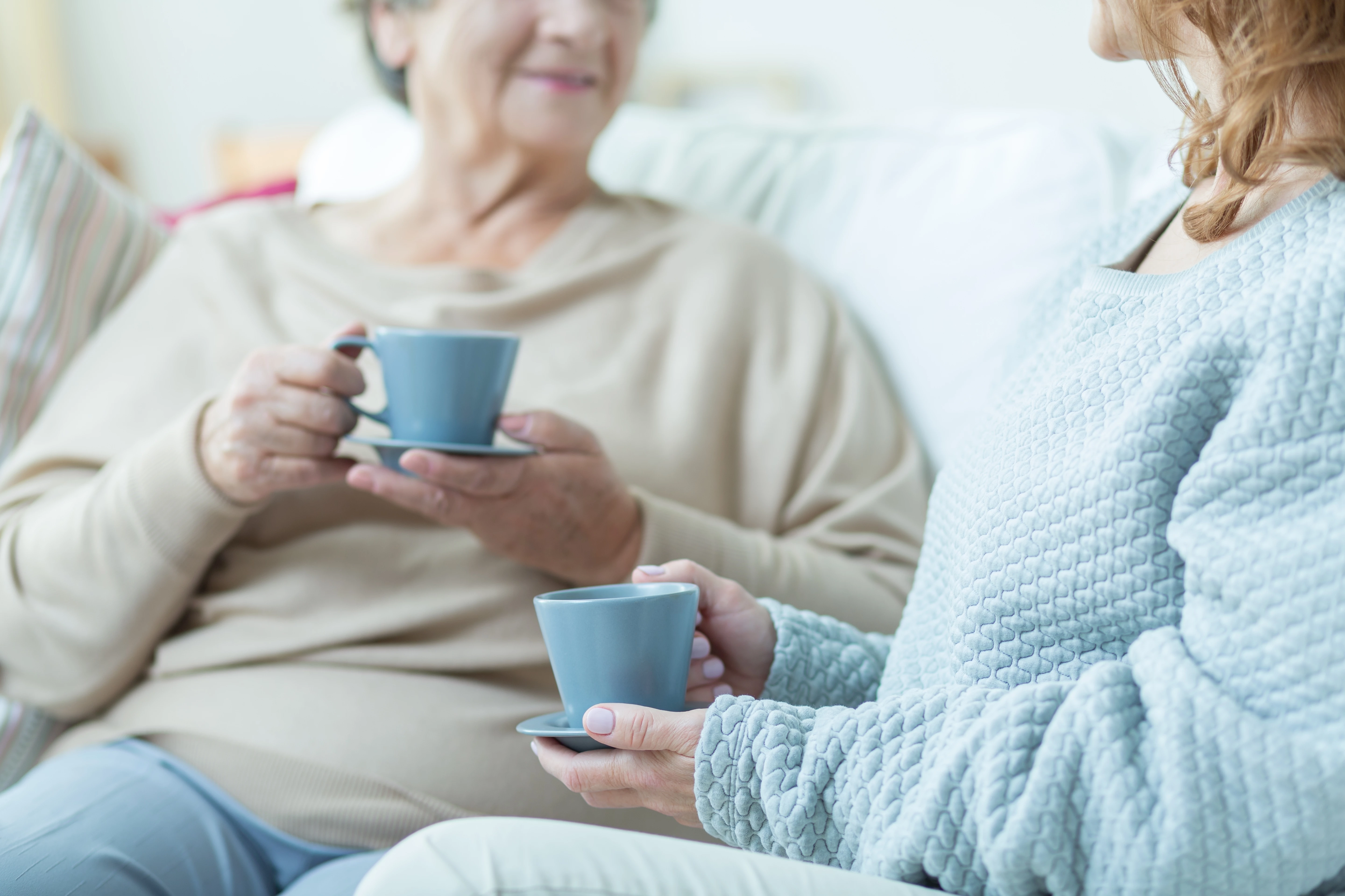 Older Woman And Younger Woman Chatting On Sofa With A Hot Drink