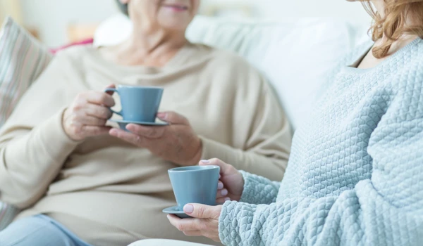 Older Woman And Younger Woman Chatting On Sofa With A Hot Drink