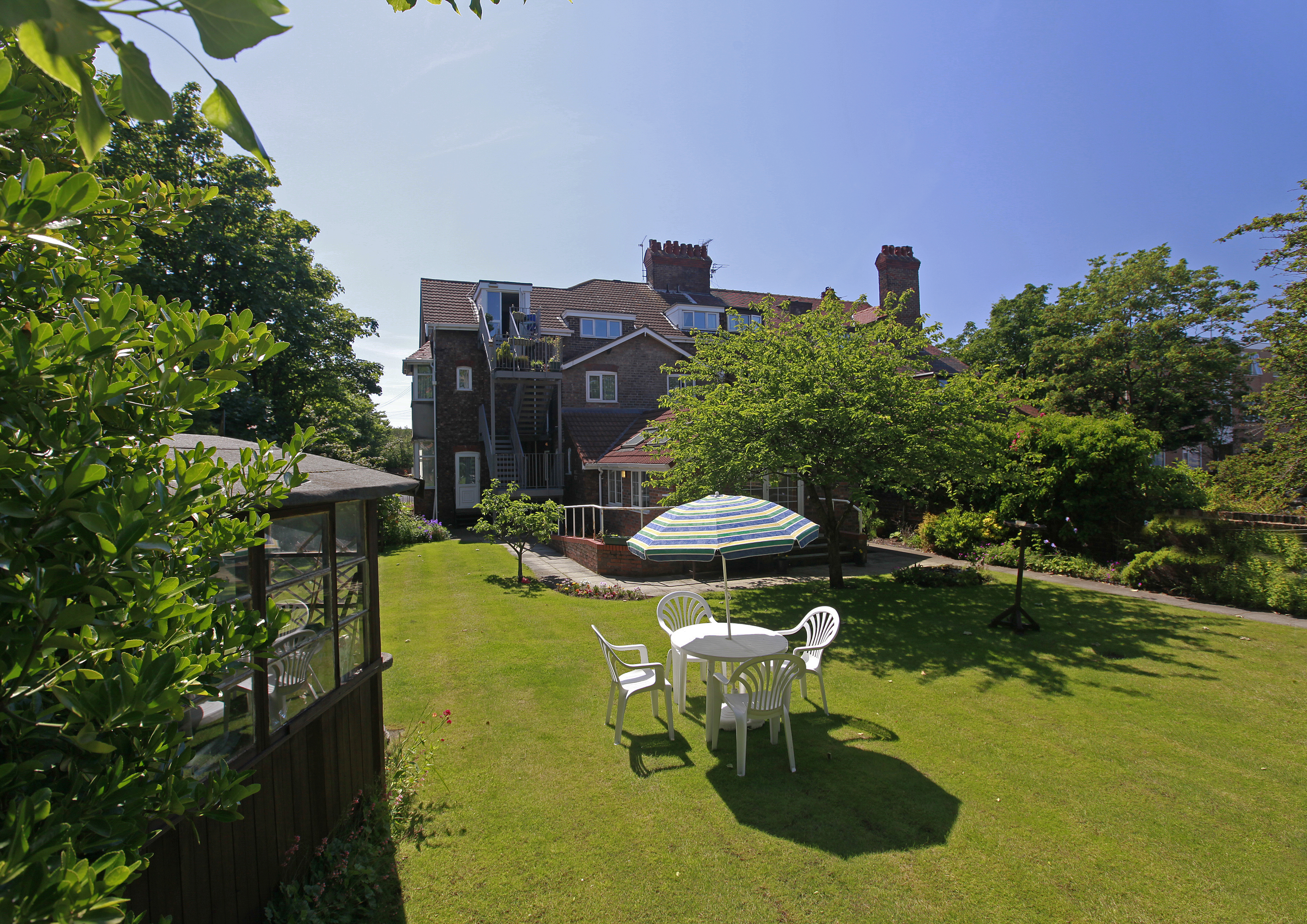 A large bright garden surrounded by trees and a patio set on the grass