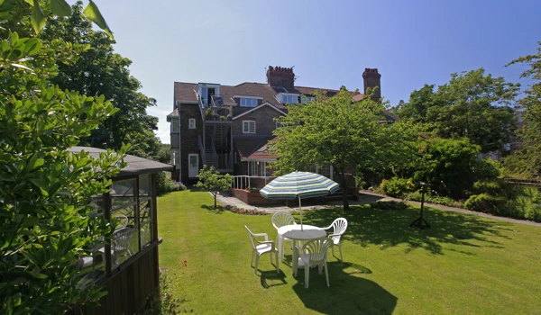 A large bright garden surrounded by trees and a patio set on the grass