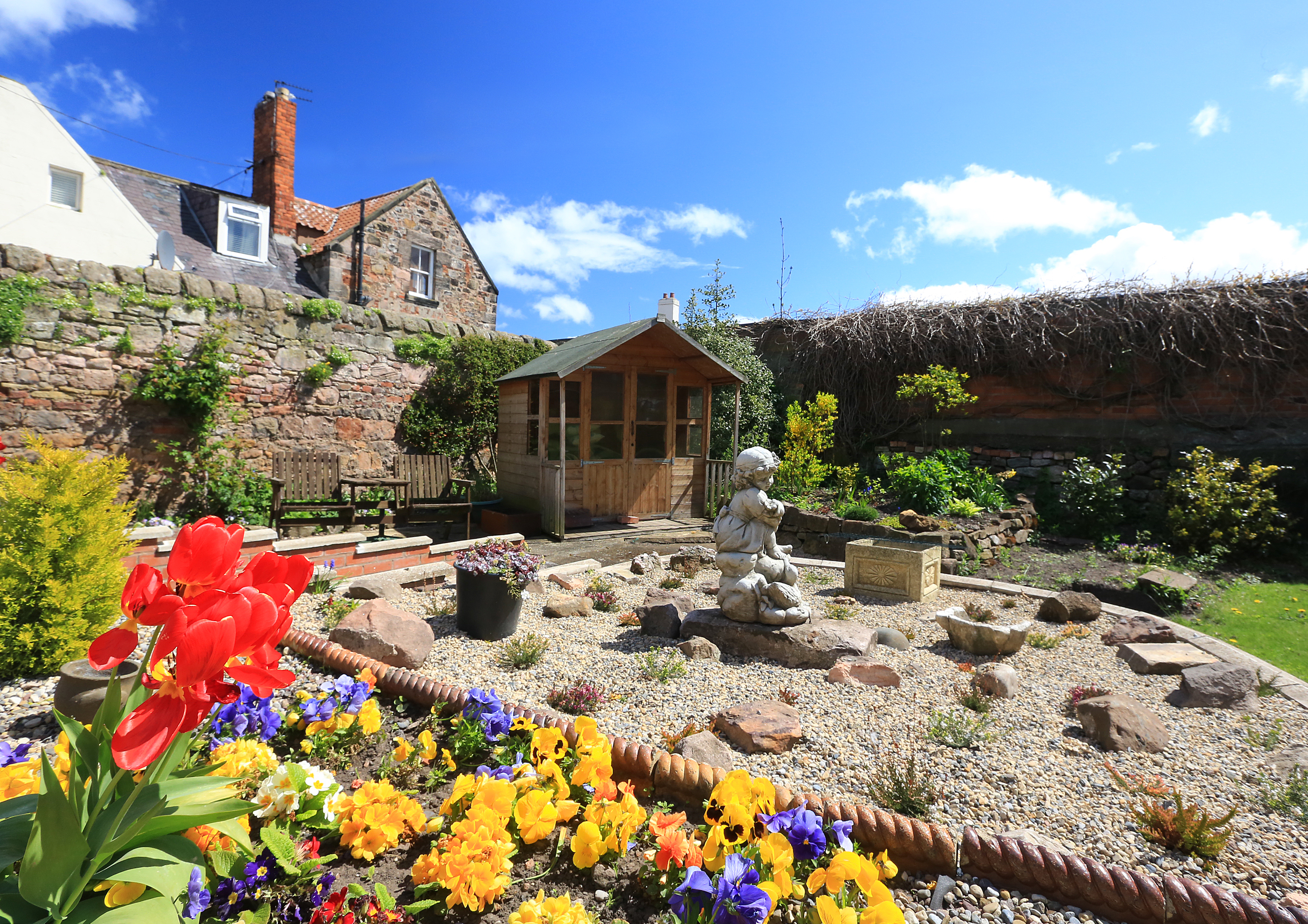 A stunning rockery in the garden with a summer house and bright flowers